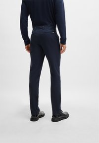 Navy chinos made of cotton blend. Slim fit with back zip pockets and belt loops. Paired with black shoes, standing on a plain background.