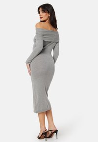 Abito grigio off-the-shoulder, silhouette aderente, maniche lunghe, lunghezza a metà polpaccio, texture a costine, abbinato a sandali neri con tacco alto.