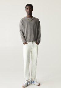 Grijs overhemd met lange mouwen, lichte spijkerbroek en grijze sneakers met blauwe accenten. De outfit heeft een relaxte pasvorm en een minimalistisch ontwerp.