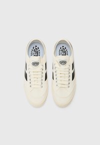 Cremefarbene Canvas-Sneaker mit schwarzen Streifen. Sie verfügen über weiße Schnürsenkel, eine strukturierte Gummisohle und ein schwarzes Logo auf der Zunge. Glatte Oberfläche.