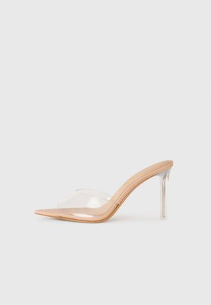 Mule bej cu toc înalt, cu curea transparentă la vârful încălțămintei și toc stiletto transparent, pe un fundal alb.