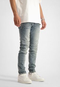 Ljust blå smala jeans med bleka områden, tillsammans med vita sneakers. Tyget ser ut att vara denim med en slät textur. Skjortan är oversized och vit.