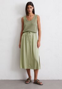 Light green tank top with textured knit, paired with a flowing, elastic waistband midi skirt and flat sandals with a buckle detail.