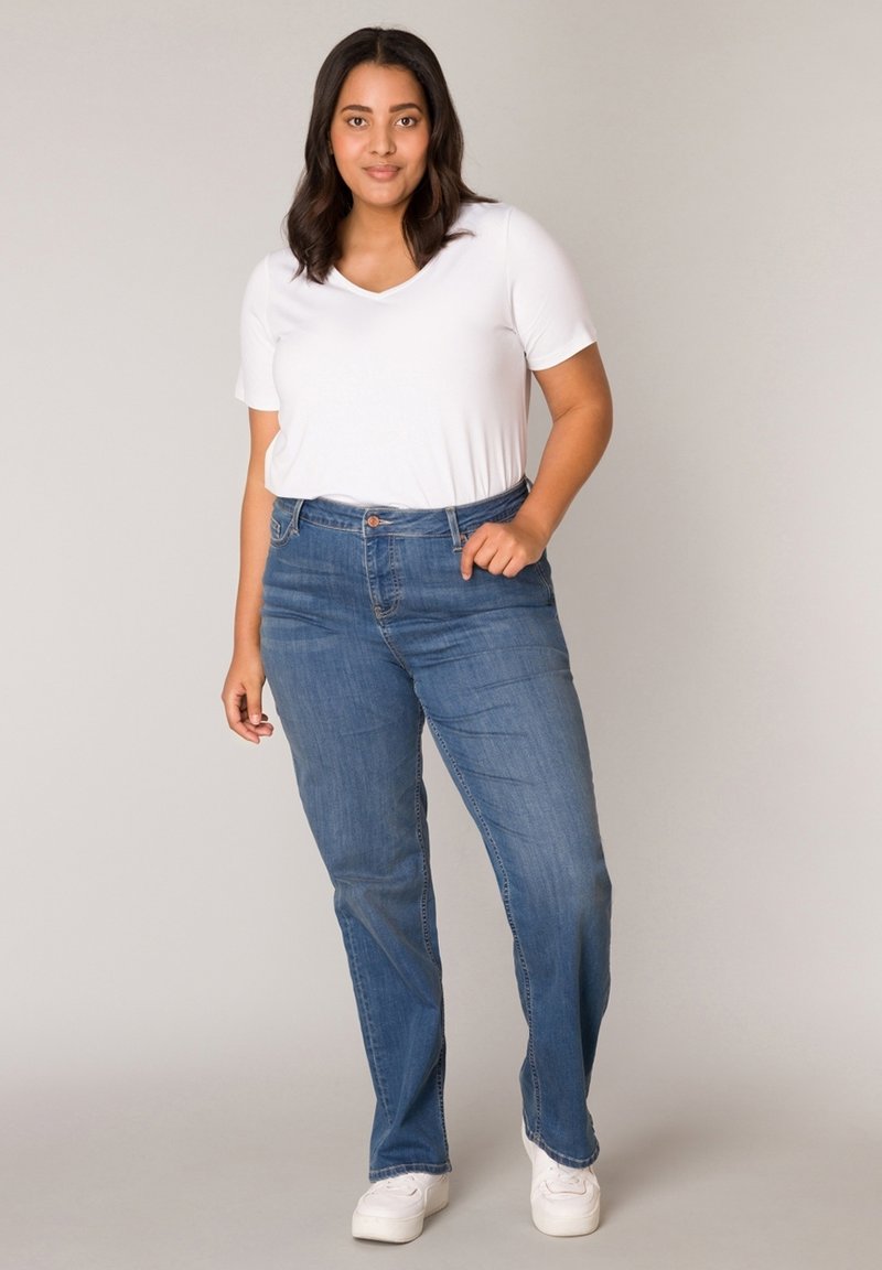 Witte korte mouwen V-hals t-shirt gecombineerd met blauwe rechte jeans, met een knoopsluiting en vijf-pocket ontwerp. Witte sneakers.