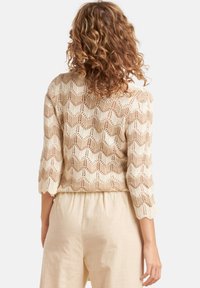 Gehaakte trui in beige met een chevronpatroon, driekwart mouwen en gegolfde randen. Lichtgewicht ontwerp met open breiwerk.