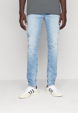 Vaqueros de mezclilla azul claro con un corte ajustado, que presentan una textura suave y un desgaste mínimo. Combinados con zapatillas blancas con rayas grises.