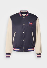 Mörkblå varsityjacka med crèmefärgade ärmar, randig ribbad krage och manschetter, broderad logotyp och tryckknappar. Två sidfickor.