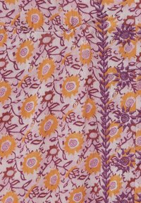 Tejido rosa claro con patrones florales en naranja y púrpura, con intrincados bordados y motivos de hojas en espiral. Detalles de costura decorativa visibles.