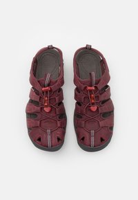 Bordeauxfarbene Sandalen mit mehreren verstellbaren Riemen, strukturierten Innensohlen und schwarzen Gummisohlen. Mit kleinen roten Akzenten und weißen Nähten.