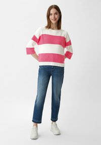 Gebreide trui met roze en witte horizontale strepen, driekwartmouwen, gecombineerd met blauwe rechttoe-rechtaan jeans en witte sneakers.