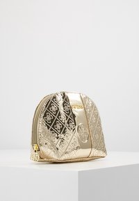 Guld metallisk kosmetiktaske med et struktureret quiltet mønster, lynlås lukning og et cirkulært præget logo på siden. Kompakt og afrundet design.