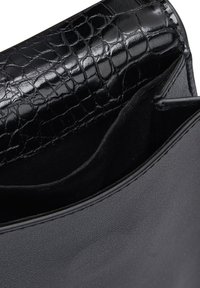Primo piano di una borsa in pelle nera con esterno liscio e dettagli in motivo coccodrillo testurizzato sul pattino.