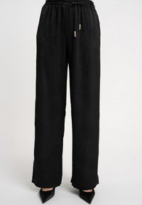 Czarne spodnie o szerokich nogawkach z połyskującą teksturą, wyposażone w elastyczny pas i sznurek do regulacji. Delikatny kwiatowy wzór i zwężane mankiety.