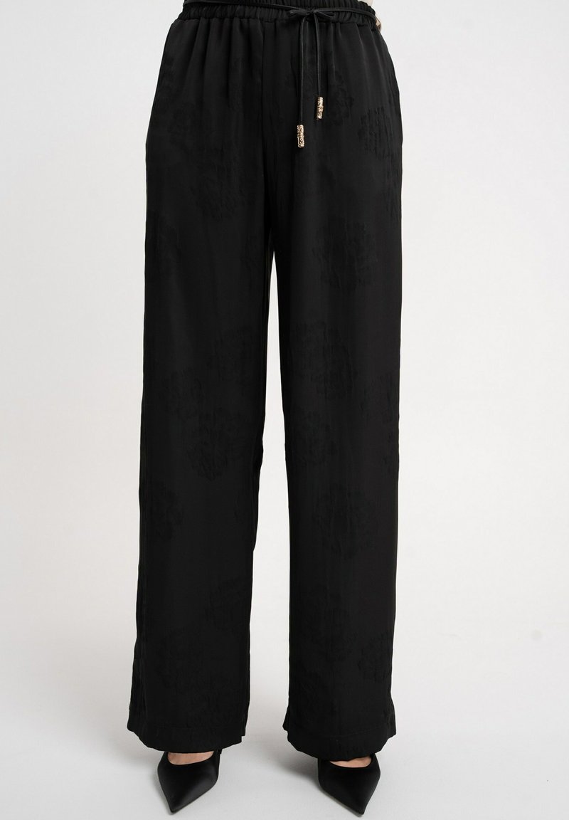 Czarne spodnie o szerokich nogawkach z połyskującą teksturą, wyposażone w elastyczny pas i sznurek do regulacji. Delikatny kwiatowy wzór i zwężane mankiety.
