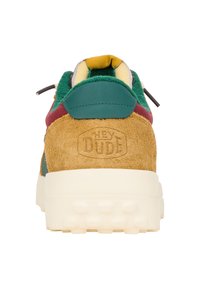 Zapatilla de ante verde y marrón con un cuello acolchado, acentos estampados y una suela blanca texturizada. Logo "HEY DUDE" grabado en la parte trasera.