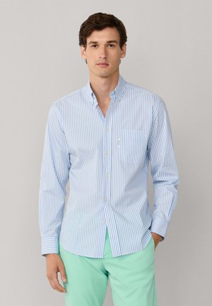 Camisa abotonada a rayas azul claro y blanca con cuello, mangas largas, un solo bolsillo en el pecho y corte ajustado. Se lleva con pantalones verde menta.