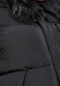 Svart puffjacka med en avtagbar fuskpälskrage, har dragkedjestängning och strukturerad textil med synliga sömmar.