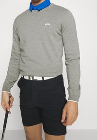 Pull gris en maille avec col rond, logo "BOSS" blanc ; superposé sur une chemise bleue à col. Short noir et ceinture blanche avec garnitures argentées.