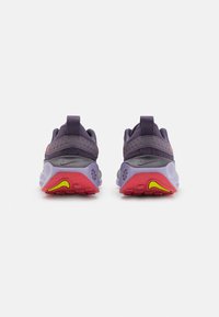 Scarpe da atletica viola con una tomaia in rete testurizzata, forma arrotondata e un accentuato suola rossa e gialla. Presentano un colletto imbottito e una linguetta sul tallone.