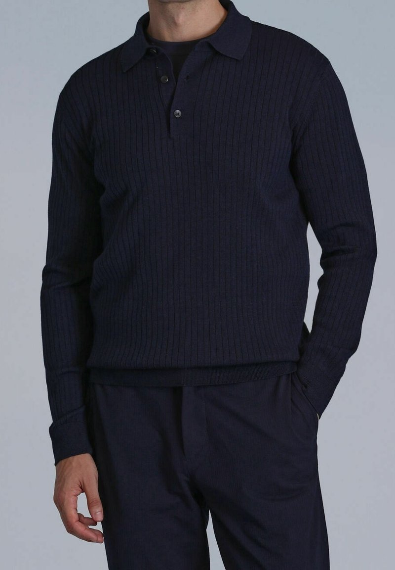 Polo à manches longues côtelé bleu marine avec une patte à deux boutons, texture tricotée et poignets contrastants, assorti à un pantalon foncé.