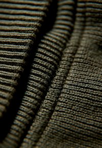 Getextureerde stof in donkergroen met horizontale strepen; close-up die variërende patronen en een zachte, vezelachtige textuur toont.