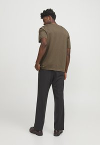 Olive green cotton t-shirt with a round neck and short sleeves, paired with black trousers and dark shoes, showing a relaxed fit.