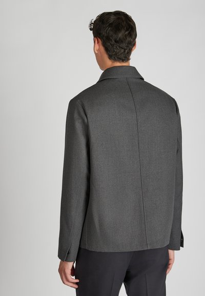 Giacca grigia con tessuto texture, schiena dritta, maniche lunghe e colletto; presenta bottoni sui polsini e un design minimalista.