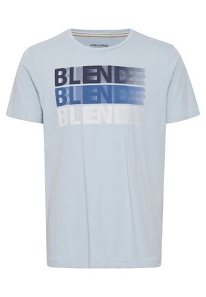 Svetlomodré tričko s krátkym rukávom vyrobené z bavlny. Má grafický potlač so prekrývajúcim sa textom "BLEND" v rôznych odtieňoch modrej a bielej.