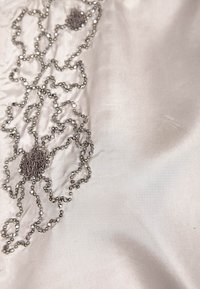 Silky cream fabric with intricate silver bead embroidery forming a swirling pattern, featuring smooth texture and subtle sheen.