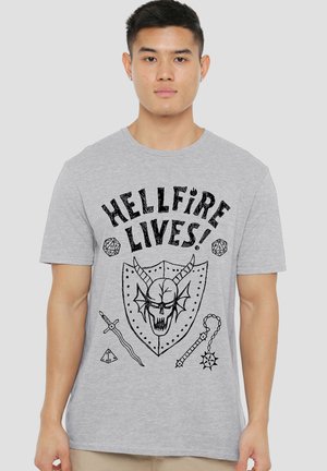 Young man wearing a gray T-shirt with text "HELLFIRE LIVES!" and graphics of a horned skull, shield, sword, dice, and flail weapon.