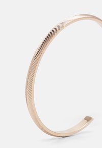Rose gold metal cuff bracelet featuring a smooth interior and an exterior textured with subtle diagonal grooves.