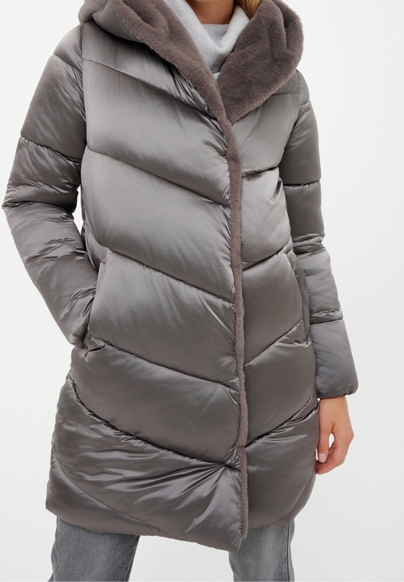 Abrigo acolchado gris con un patrón en forma de cheurón, que cuenta con una capucha suave forrada de piel y ribetes contrastantes. El material tiene un acabado brillante.