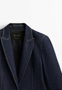 Veste blazer en jean bleu foncé avec surpiqûres contrastantes, revers crantés et doublure intérieure noire avec une étiquette Massimo Dutti visible.