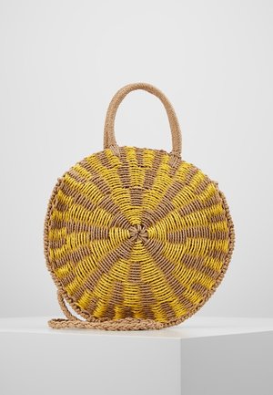 Round woven straw handbag with yellow and natural brown zigzag pattern, top handle, and braided shoulder strap on white surface.