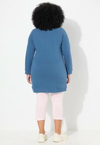 Robe sweat bleue à manches longues, avec des poignets et un ourlet côtelés. Portée avec des leggings capri rose clair et des baskets beiges. Texture de tissu lisse.