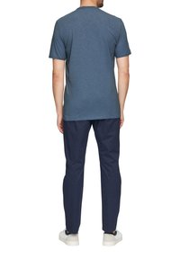 Męska niebieska koszula z krótkim rękawem, wykonana z lekkiego materiału, w połączeniu z ciemnoniebieskimi spodniami i białymi trampkami, widok z tyłu.