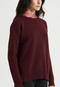 Bordeauxroter Pullover mit klassischem Rundhalsausschnitt, geripptem Saum und Bündchen, leicht lockerer Passform und strukturierter Strickware.