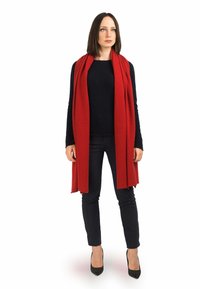 Rød tørklæde lavet af blødt materiale, hængende løst om halsen over en sort sweater og bukser, parret med sorte høje hæle.