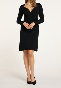 Robe noire à manches longues avec un décolleté en V profond, un corsage ajusté et un ourlet légèrement évasé. Confectionnée dans un tissu doux avec une texture subtile.