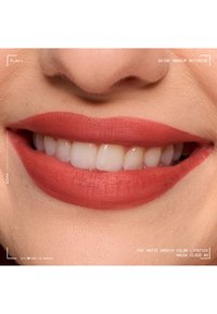 Close-up of lips with smooth mauve matte lipstick and visible white teeth in a slight smile, showing natural skin texture around the mouth.