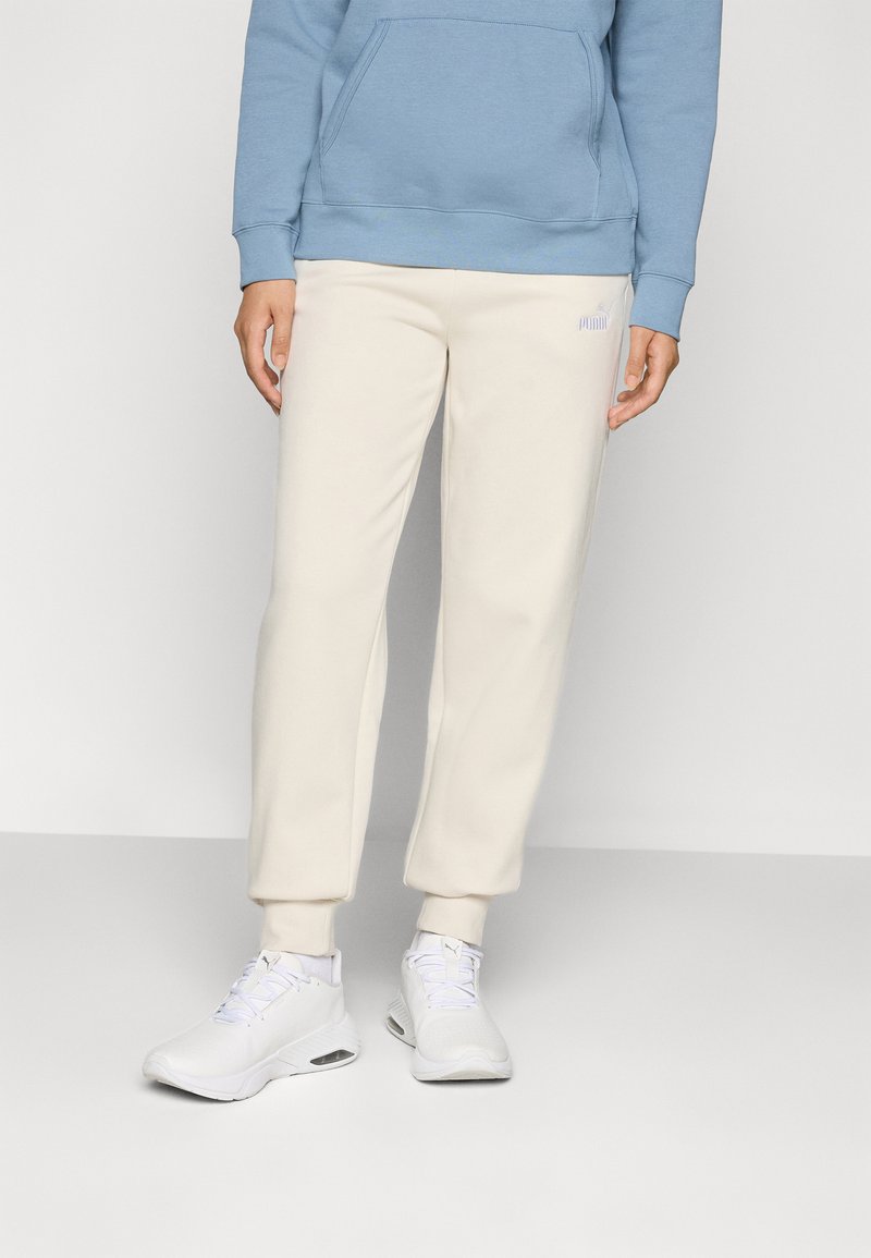 Hellbeige Jogginghosen mit schmal zulaufenden Beinen und elastischen Bündchen, kombiniert mit weißen Sportschuhen. Darüber wird ein blauer Hoodie getragen, der eine Fronttasche hat.
