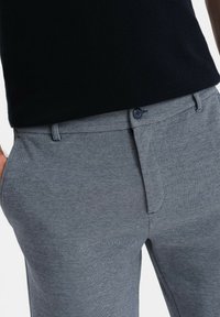 Šedé texturované kalhoty s jemným vzorem rybí kosti, obsahující přední kapsu, zapínání na knoflík a poutka na opasek.