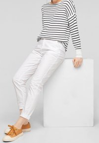 Pantaloni bianchi di cotone abbinati a un maglione a righe bianche e nere. Sneakers marrone-arancione con suola texturizzata. Design semplice e informale.