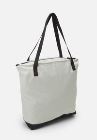 Sac fourre-tout en tissu durable, avec un corps gris clair et un fond gris foncé. Il possède de longues poignées noires et une fermeture éclair.