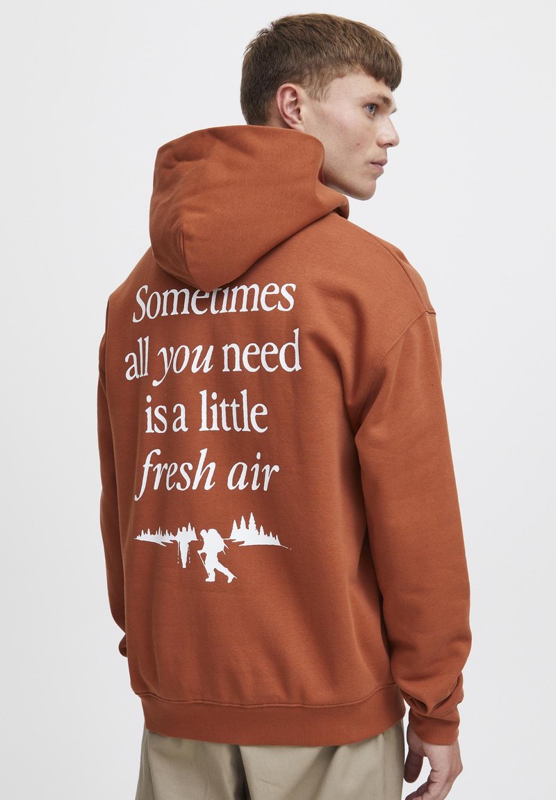 Sudadera marrón con capucha ajustable, que presenta un texto blanco: "A veces lo único que necesitas es un poco de aire fresco" y gráficos de senderismo en la parte posterior.
