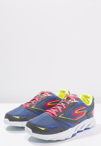 Baskets de sport avec tige en mesh bleu marine, accents gris, lacets roses et détails jaune vif. Semelle blanche épaisse avec bande de roulement texturée.