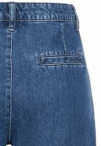 Denim jeans met een donkerblauwe wassing, een tailleband met riemlussen en een enkele achterzak zonder zichtbare hardware of versieringen.