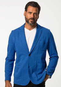 Blazer blu da uomo realizzato in tessuto testurizzato con chiusura a un bottone, due tasche davanti e colletto a punta. Indossato sopra una t-shirt bianca.
