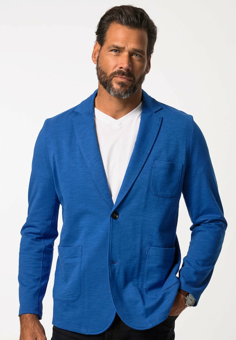 Herrblazer i blått, tillverkad av texturerat tyg med en knäppning fram med en knapp, två framfickor och slagkrage. Bärs över en vit t-shirt.
