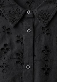 Camicia nera ricamata con motivi floreali a intaglio, colletto e dettagli con bottoni sulla parte anteriore, realizzata in tessuto texturizzato.